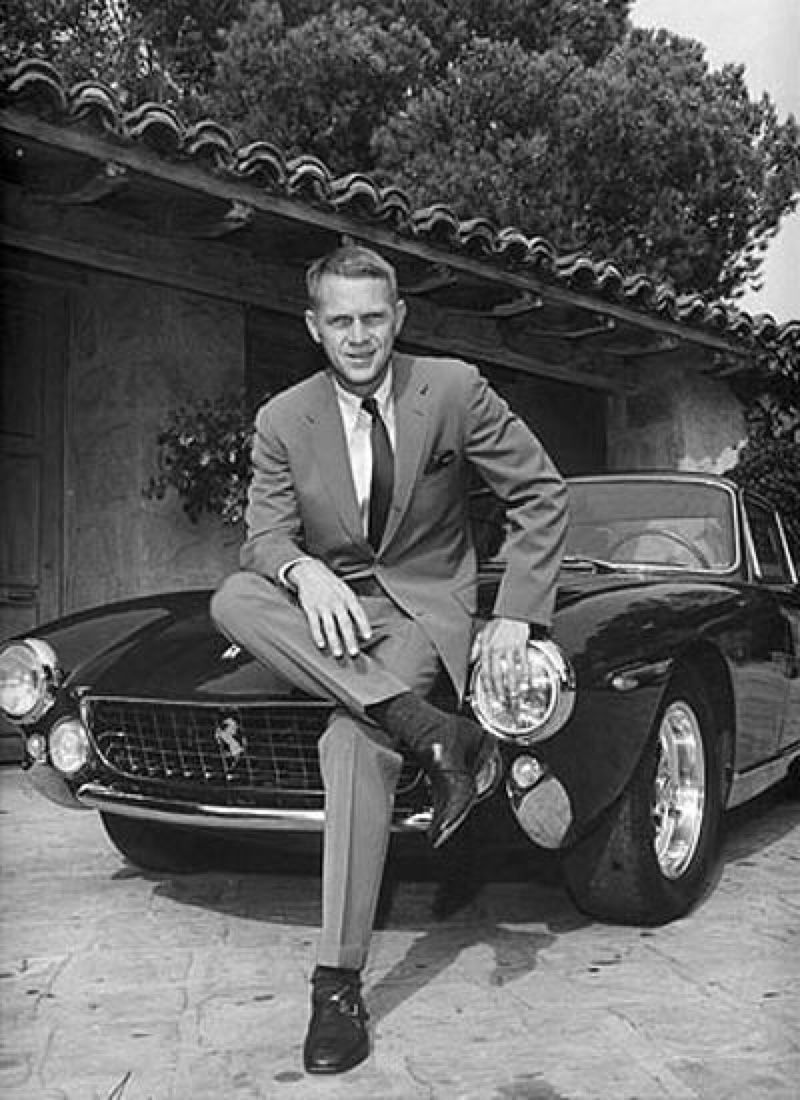 Steve McQueen sitting in front of a Ferrari 1